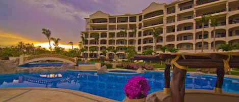 A resort with a large pool, palm trees, and a multi-story building with balconies.