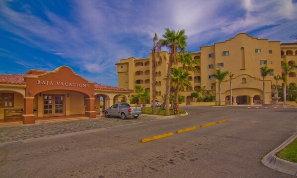 L’entrée d’un hôtel, avec une enseigne indiquant « BAJA VACATIONS », et une allée pavée menant à l’aire de stationnement.