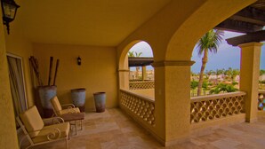A covered patio area with seating, large vases, and a view of a resort with palm trees. - Las Mananitas LM F4205 2 Bedroom Condo By Seaside Los Cabos (San José del Cabo)