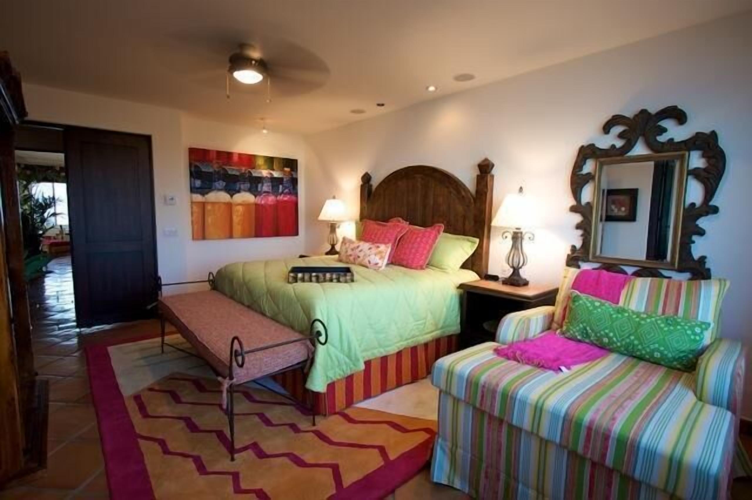 A bedroom with two beds, a bench, a striped chair, and a mirror.