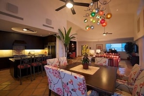 A spacious living area with a dining table, floral chairs, a ceiling fan, and a decorative light fixture.