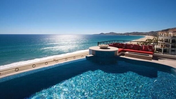 Una piscina con agua azul cristalina, un área de descanso roja y vistas al océano y la playa.