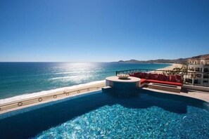 A pool with clear blue water, a red seating area, and a view of the ocean and beach. - Tortuga Bay TBA 1601 4 Bedroom Condo By Seaside Los Cabos (San José del Cabo)