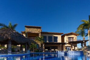 Un complexe hôtelier doté d’une piscine, d’une structure à toit de chaume et d’un immeuble à plusieurs étages avec des balcons.
