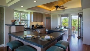 A modern kitchen with a central island, seating area, and a view to the outdoors. - Palm Villa 126B (Kailua-Kona)