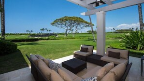 A patio with outdoor furniture, a view of a golf course, and a large tree. - Palm Villa 126B (Kailua-Kona)