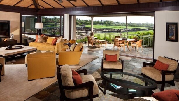 A spacious living area with a large sofa, armchairs, and a coffee table, featuring a scenic view of a golf course through large windows. - 115D Waiulu Street Hualalai (Kailua-Kona)