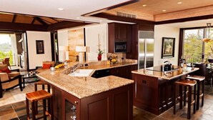 A spacious kitchen with granite countertops, dark wood cabinets, and stainless steel appliances. - 115D Waiulu Street Hualalai (Kailua-Kona)
