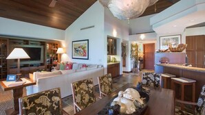 A spacious living room with a wooden ceiling, a dining area with a table set for four, and a kitchen visible in the background. - 120A Waiulu Street Hualalai (Kailua-Kona)