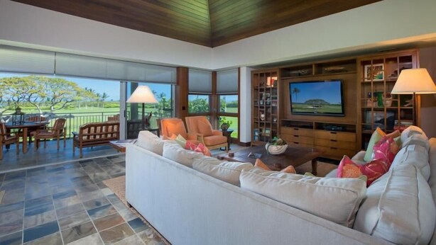 A spacious living room with a large sofa, a television, and a dining area with chairs and a table. - 120A Waiulu Street Hualalai (Kailua-Kona)