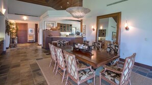 A spacious dining area with a large wooden table and matching chairs, a chandelier, and a kitchen in the background. - 120A Waiulu Street Hualalai (Kailua-Kona)
