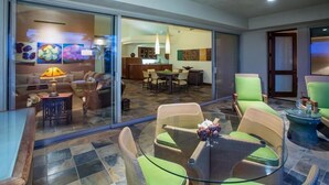 A modern living area with a glass partition, wicker furniture, a dining table, and a kitchen in the background. - 104A Waiulu Street Hualalai (Kailua-Kona)