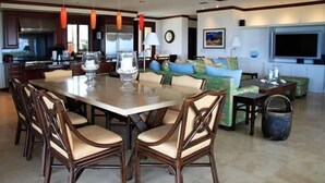 A spacious living area with a large dining table surrounded by chairs, a sofa set, a television, and a kitchen in the background. - Wai ula ula344 (Kamuela)