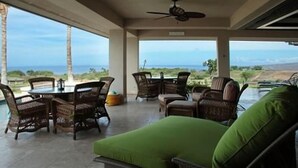 A covered outdoor seating area with wicker furniture and a green cushion, overlooking a scenic view. - Wai ula ula344 (Kamuela)