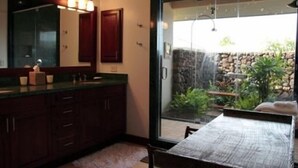 A bathroom with a large mirror, wooden cabinets, and a view of a garden through a glass door. - Wai ula ula344 (Kamuela)