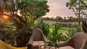 A wicker chair and table set outdoors with a view of a golf course and lush greenery. - 129B Hualalai (Kailua-Kona)