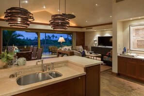 Uma cozinha moderna com uma ilha grande, uma sala de jantar com televisão e vista para palmeiras.