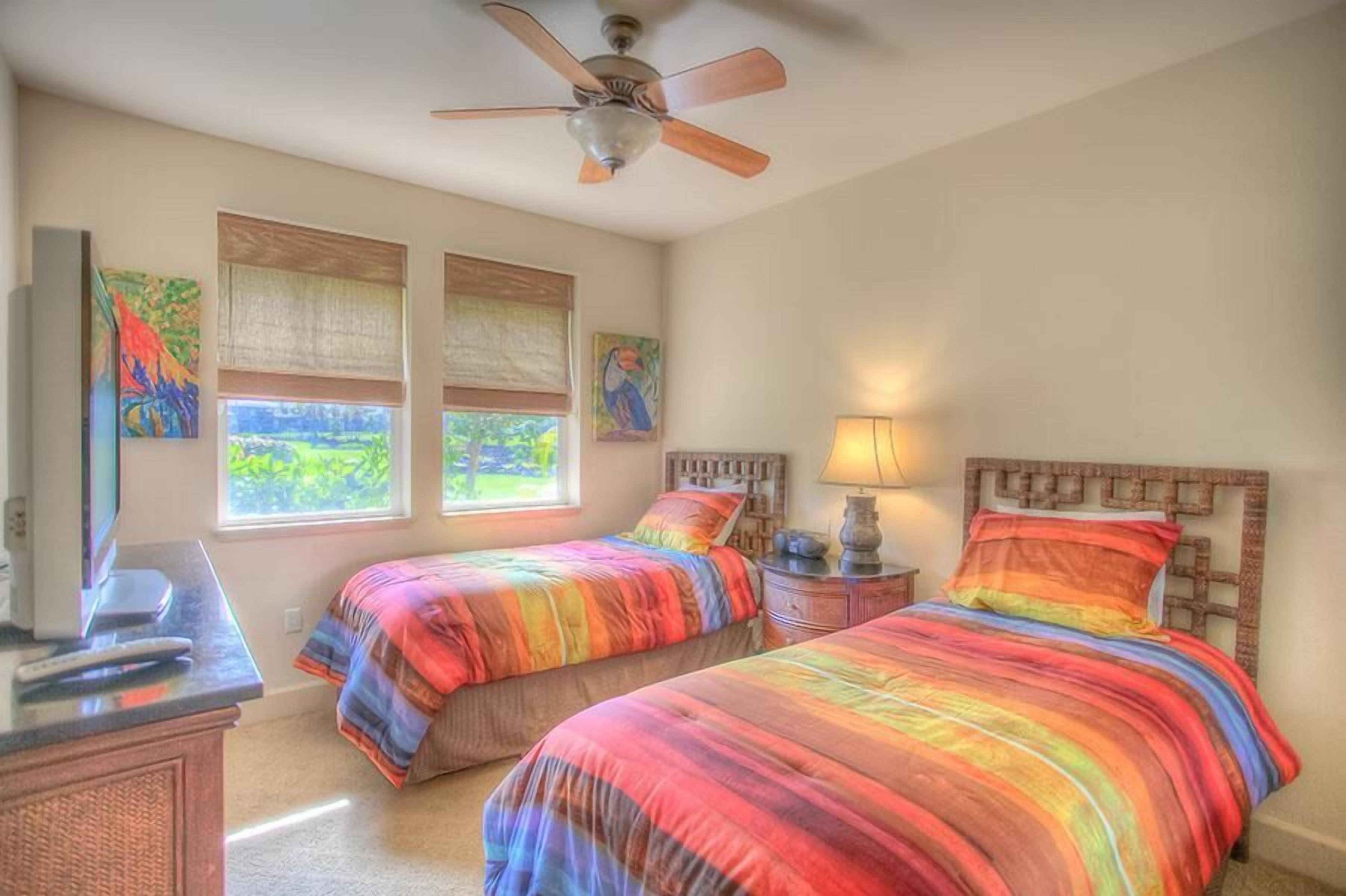 A bedroom with two beds, a ceiling fan, a TV, and artwork on the walls.