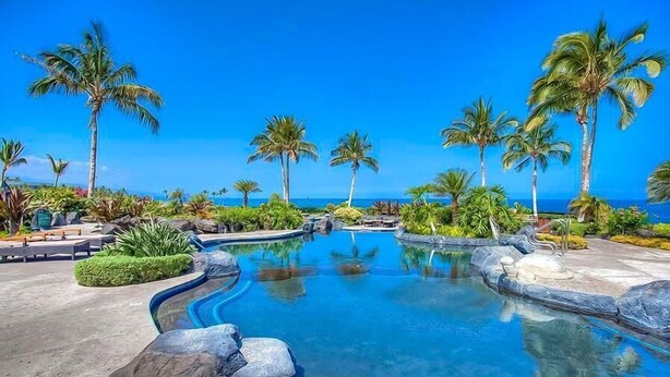 A pool area with palm trees and a view of the ocean.