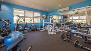 A gym with exercise equipment, large windows, and a blue wall. - Fairways at Mauna Lani 1305 (Kamuela)