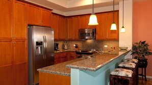A kitchen with wooden cabinets, stainless steel appliances, granite countertops, and pendant lighting. - Fairways at Mauna Lani 1104 (Kamuela)