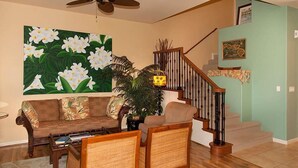 A living room with a sofa, chairs, a coffee table, a painting, a staircase, and a ceiling fan. - Fairways at Mauna Lani 1104 (Kamuela)