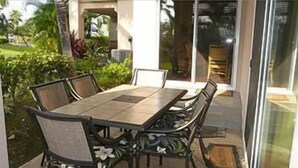 Eine Terrasse im Freien mit einem rechteckigen Tisch und sechs Stühlen, umgeben von üppigem Grün.