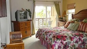 Ein Schlafzimmer mit Bett, Kommode, Fernseher und einem Balkon mit Stuhl.