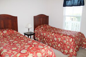 A bedroom with two wooden headboards, a nightstand with a lamp, and a window with blinds.