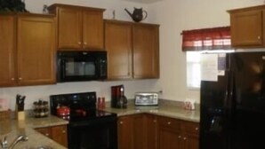 Una cocina con armarios de madera, un microondas negro, un tostador y un refrigerador.