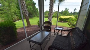 A covered patio with a table and two wicker chairs, overlooking a well-maintained lawn and trees. - 1715 Willow Bend (North Myrtle Beach)
