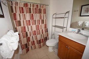 Un baño con cortina de ducha, inodoro, lavabo con espejo y toallero.