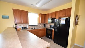 A kitchen with wooden cabinets, a black refrigerator, a microwave, and a stove. - 1715 Willow Bend (North Myrtle Beach)