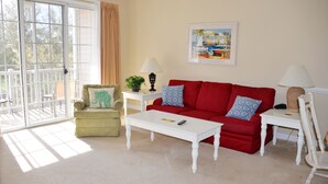 A living room with a red sofa, a white coffee table, a green armchair, and a white side table with a lamp. - 1523 The Havens (North Myrtle Beach)