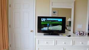 A television on a white dresser with drawers, a remote control, and a small framed picture above it. - 1523 The Havens (North Myrtle Beach)