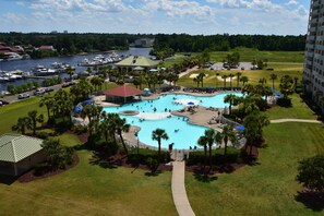 A large outdoor swimming pool surrounded by palm trees and a marina with boats. - 1805 Yacht Club Villas (North Myrtle Beach)