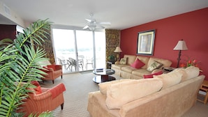 A living room with a beige sofa, a red armchair, a coffee table, and a large plant. - 1805 Yacht Club Villas (North Myrtle Beach)