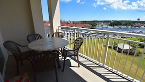 A balcony with a table and chairs, overlooking a marina with boats and a cityscape in the distance. - 1805 Yacht Club Villas (North Myrtle Beach)