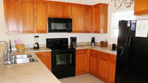 Una cocina con armarios de madera, un microondas negro, una estufa negra, un refrigerador y un lavamanos.