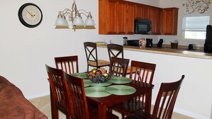 Un comedor con una mesa de madera, sillas, una araña y un reloj en la pared.