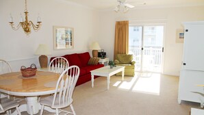 A living room with a dining table, chairs, a red sofa, a green armchair, a white refrigerator, and a balcony with a view. - 223 Willow Bend (North Myrtle Beach)