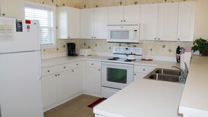 A kitchen with white cabinets, a microwave, a stove, a sink, and a window with blinds. - 223 Willow Bend (North Myrtle Beach)