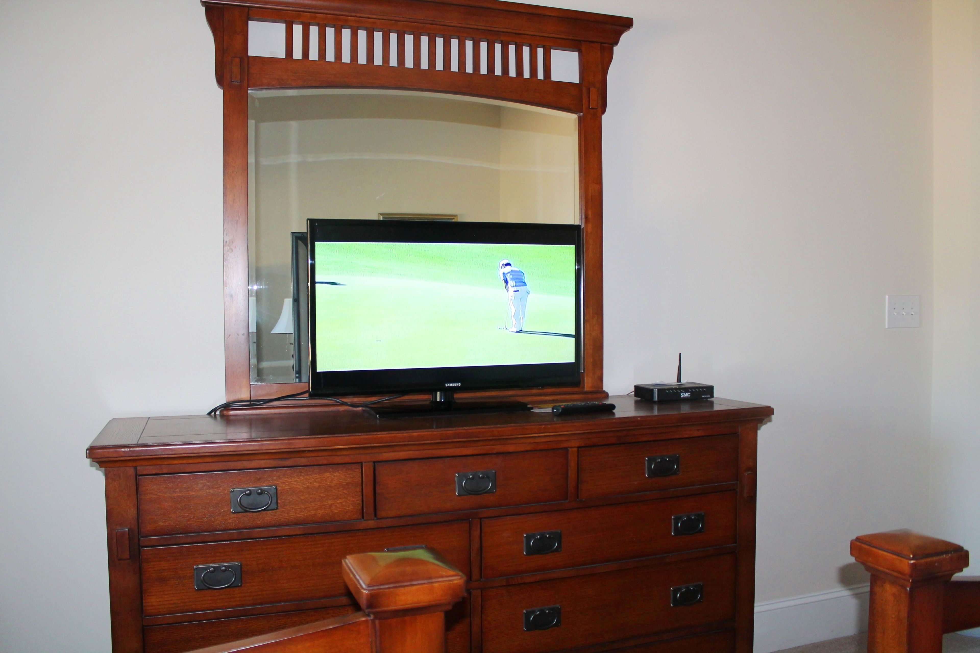 A wooden dresser with a television on top, drawers, and a mirror above the TV.