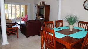 Un comedor con una mesa de madera dispuesta para cuatro personas, rodeada de sillas a juego. Hay una planta en maceta sobre la mesa y una estantería al fondo.
