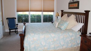 Un dormitorio con una cama grande, una silla, una mesita de noche y una ventana con persianas.