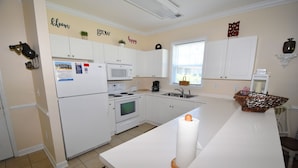 A modern kitchen with white cabinets, a refrigerator, a microwave, and a stove. There are decorative wall stickers and a basket on the counter. - 411 Willow Bend (North Myrtle Beach)
