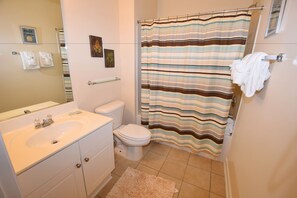 A bathroom with a white sink, toilet, and striped shower curtain. - 411 Willow Bend (North Myrtle Beach)