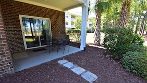A covered patio with a brick wall, sliding glass doors, and a table with chairs. - 411 Willow Bend (North Myrtle Beach)