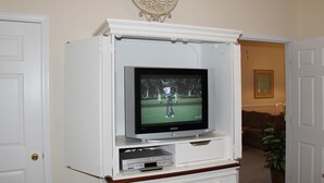 Ein Wohnzimmer mit Fernseher auf einem weißen Unterhaltungsschrank, einer Tür und einem gerahmten Bild an der Wand.