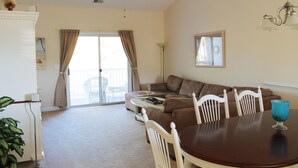 Ein Wohnzimmer mit braunem Sofa, weißen Stühlen, einem Esstisch und einem Deckenventilator.